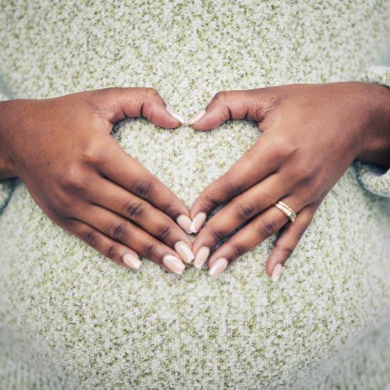 En kvinder laver et hjerte med sine hænder på sin gravide mave