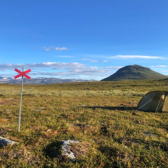 Et telt og et vandreskilt står flot med et bjerg i baggrunden