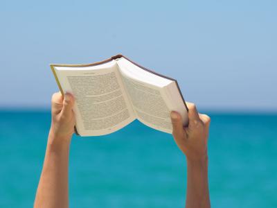En person holder en åben bog op, baggrunden er havet og horisonten
