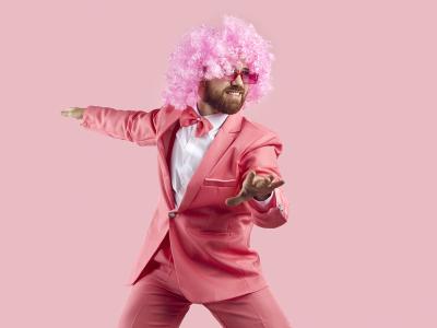 En mand i et lyserødt jakkesæt, med lyserød paryk danser foran en lyserød baggrund