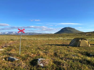 Et telt og et vandreskilt står flot med et bjerg i baggrunden